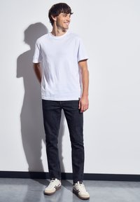 Bílý krátký rukáv tričko, tmavé slim-fit džíny a béžové tenisky s tmavými akcenty. Jednoduchý design s volným střihem.