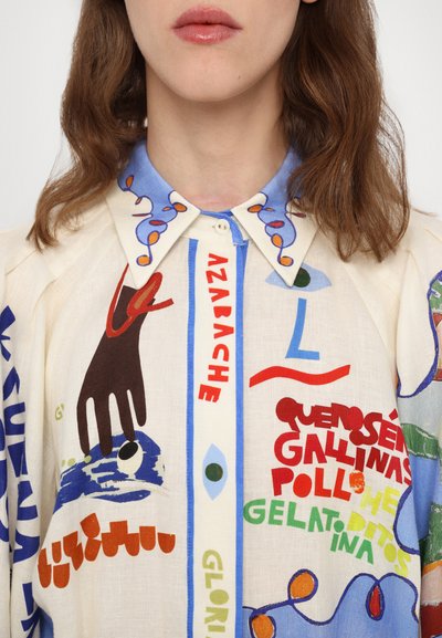 Kreminės spalvos marškiniai su mėlynu apykakle, puošti spalvingais abstrakčiais raštais ir tekstu raudona, žalia bei mėlyna spalvomis. Mygtukų uždarymas prie kaklo.