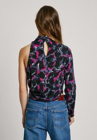 Top senza maniche floreale con motivi neri, rosa e blu; presenta una parte posteriore a chiave con chiusura a bottone. Abbinato a jeans blu.