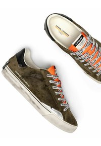 Sneaker in suede marrone con suole bianche, dettagli neri sul tallone, linguetta arancione e lacci bianchi stampati con il testo "CRIME SNEAKERS".