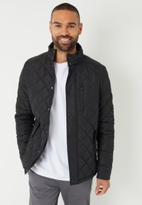 Veste matelassée noire avec col montant, dotée de fermetures à pression et à zip, d'une poche poitrine et d'une texture lisse et résistante à l'eau.