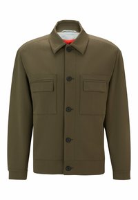 Olijfgroene jas met een knoopsluiting aan de voorkant, twee borstzakken, een kraag en een gestructureerde stof. Zwarte knopen versterken het ontwerp.