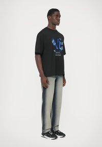 Černé oversized tričko s modrou grafikou a textem, doplněné o světle šedé džíny s již vybledlým efektem. Celý outfit doplňují černé tenisky.