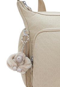 Beige backpack with a textured finish, featuring a front pocket and a plush monkey-shaped keychain attached with a silver chain.
