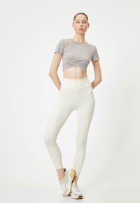 Top corto grigio chiaro abbinato a leggins bianchi a vita alta e scarpe da ginnastica chiare, realizzato in un tessuto morbido e elasticizzato.
