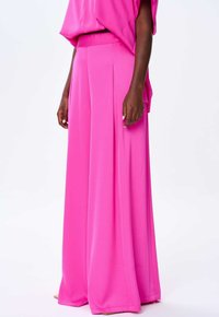 Różowe spodnie o szerokich nogawkach, wykonane z gładkiego materiału, z przodu posiadające fałdy i wysoki stan, w zestawie z pasującą luźną bluzką.