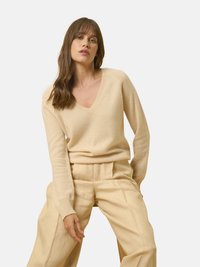 Beige V-Ausschnitt-Pullover aus weichem Material, kombiniert mit hellbeigen, weitgeschnittenen Hosen. Einfaches Design mit gerippten Bündchen und Saum.