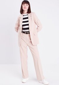 Blazer beige chiaro sopra una maglietta a righe bianco e nere. Pantaloni beige a gamba larga abbinati a sneakers bianche. Design semplice e linee pulite.