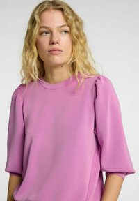 Top rosa a maniche corte con texture liscia, caratterizzato da maniche arricciate e collo rotondo. Design semplice con vestibilità comoda.