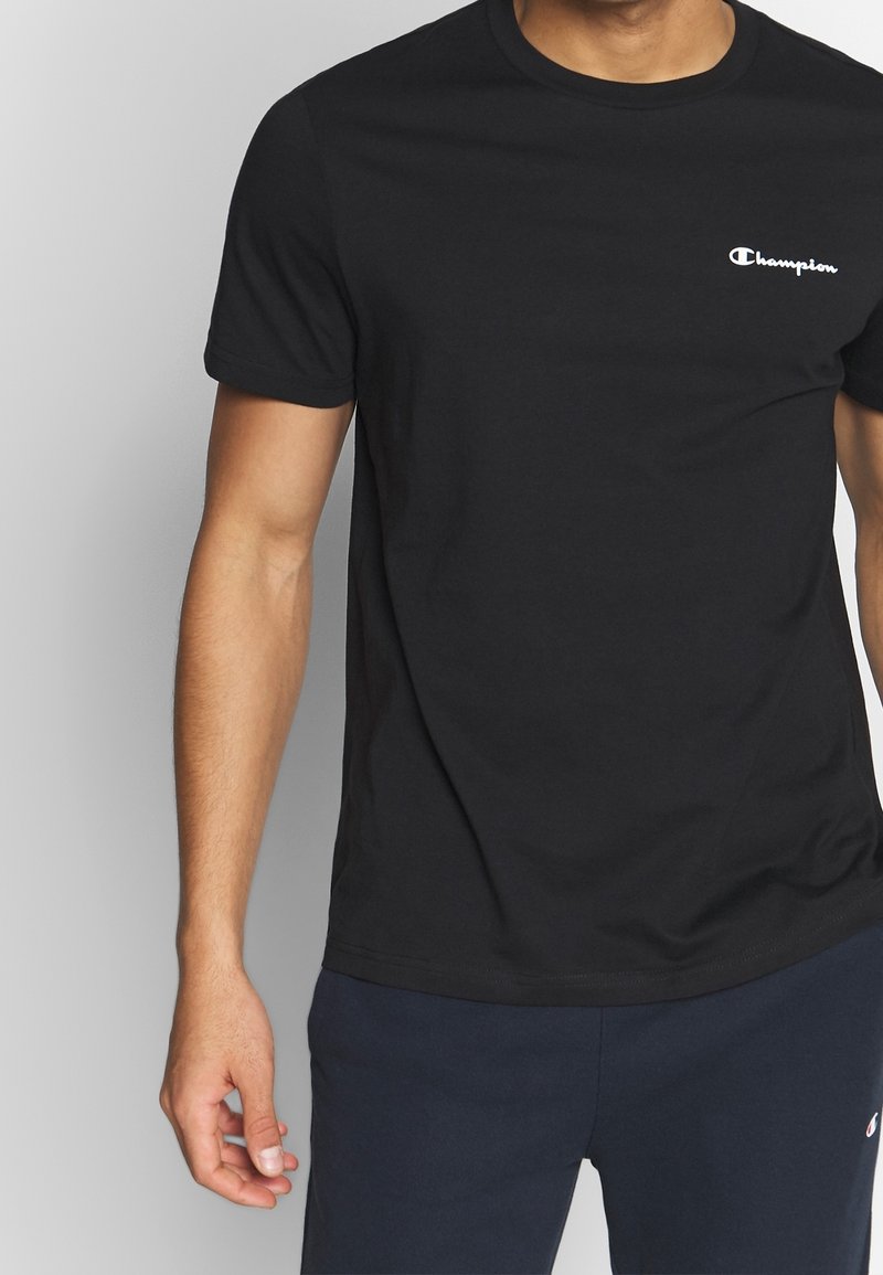 Sort bomulds t-shirt med korte ærmer, rund halsudskæring og et hvidt "Champion" logo på venstre bryst. Glat tekstur.