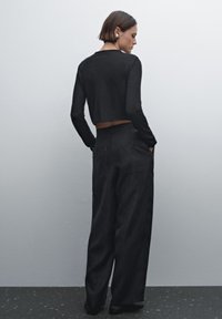 Svart kortärmad topp och vida byxor i mjukt tyg. Outfiten har en midjehöjd med medelhögt liv och bakfickor.