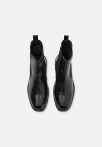 Botas de tobillo de cuero negro con un acabado liso, paneles laterales elásticos y un lazo para facilitar el calzado. Punta redondeada y suela plana de goma.