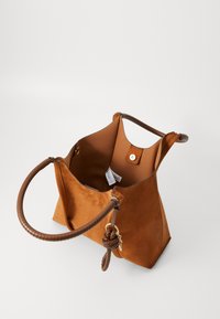 Borsa tote in suede marrone con forma strutturata, manici in pelle liscia e un charm decorativo intrecciato. Interno aperto con chiusura a scatto.