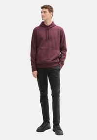 Bordeaux hoodie met een kangoeroezak, trekkoord capuchon en geribbelde manchetten, gecombineerd met zwarte broeken en zwarte lage schoenen.