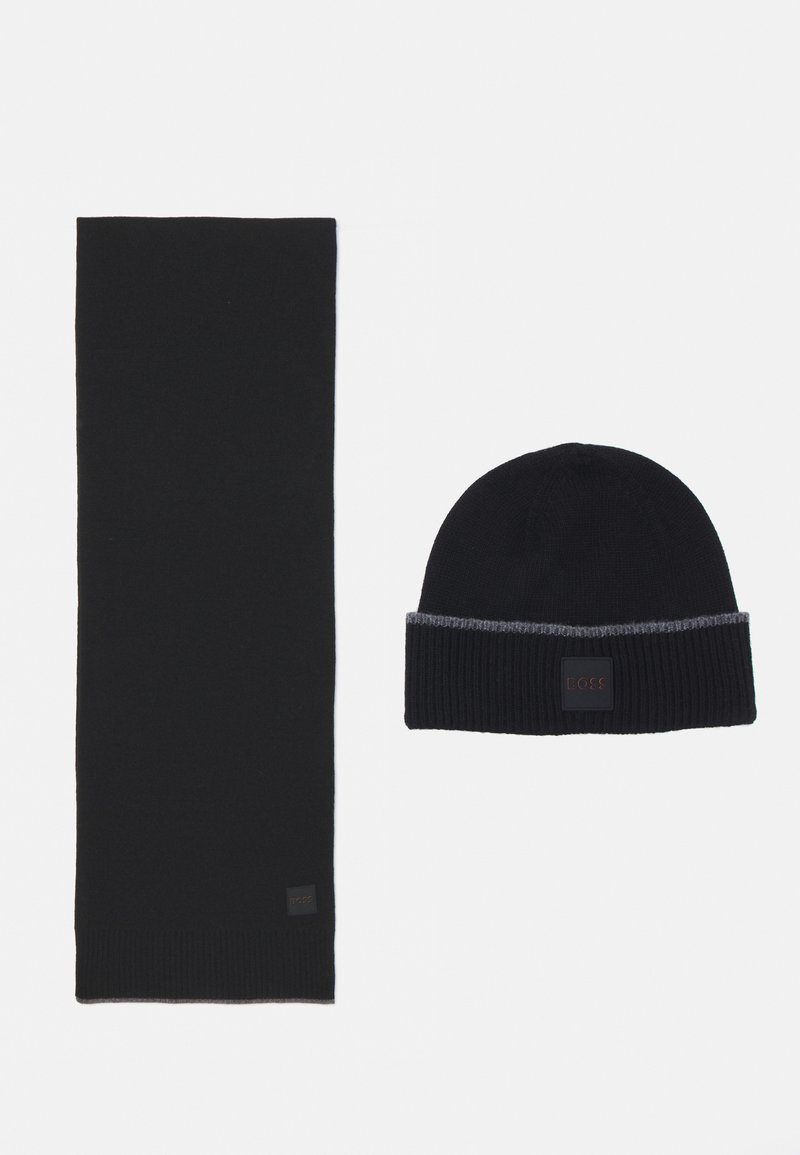 Set di sciarpa e berretto lavorati a maglia neri, con una texture a coste. Il berretto ha una fascia a righe grigie e un'etichetta con il logo. Materiale liscio, design classico.