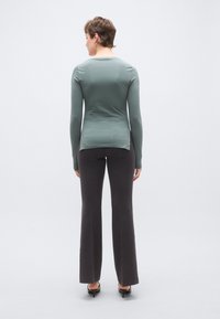 Hosszú ujjú, testhezálló felső tompa zöld anyagból, bővül�ő, sötétszürke nadrággal párosítva. A felső hátul finom hasítékkal rendelkezik az alján.