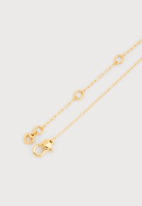 Κολιέ με χρυσή αλυσίδα και οβάλ κρίκους, με κούμπωμα σε σχήμα καρδιάς και ένα μικρό κρεμαστό στολίδι καρδιάς κοντά στο κούμπωμα.