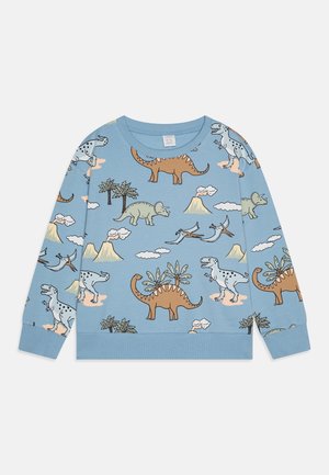 Langærmet lyseblå skjorte med tegneserie-dinosaurer, vulkaner, skyer og palmer trykt over det hele.