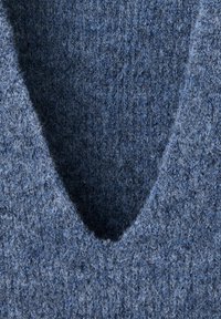 Gros plan d’un tissu tricoté bleu doux et duveteux avec un motif en V visible au niveau de l’encolure et des fibres de laine texturées.
