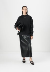 Black hoodie with patterned sleeves, paired with a black leather skirt. Model holds a black clutch and wears black heeled mules.