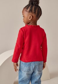 Rød langærmet skjorte med flæsekrave, parret med lyseblå denim jeans. Skjorten har en struktureret overflade.
