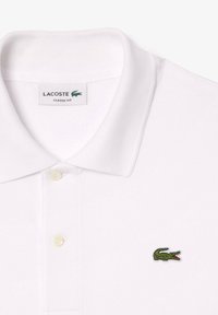 White Lacoste classic fit polo shirt with green crocodile logo on the chest and two buttons below the collar.