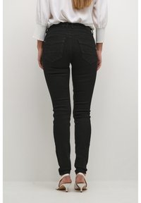 Svarta smala jeans med hög midja, med bakfickor i diamantform. Matchas med vita högklackade mules.