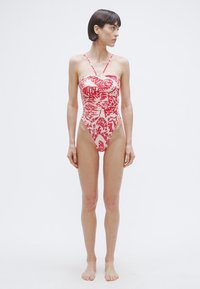 Bañador de una pieza rojo y blanco con diseño sin tirantes, textura fruncida y patrones abstractos audaces. Aperturas de pierna de corte alto.