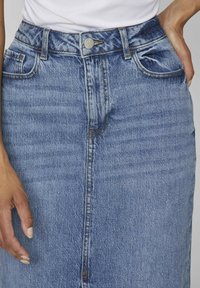 Denim skirt in light blue with a straight cut, front button closure, and two side pockets, featuring visible stitching and a textured finish.