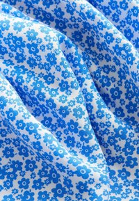 Katoenen stof met een repetitief bloemmotief in verschillende tinten blauw op een witte achtergrond, met een gladde textuur en een gedrapeerd uiterlijk.