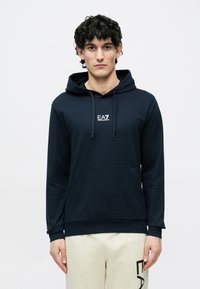 Felpa con cappuccio blu navy in cotone con tasca a marsupio frontale, cappuccio con coulisse e logo EA7 bianco sul petto. Tessuto liscio, vestibilità comoda.