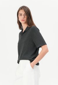 Mörkgrå kortärmad polo med krage och tvåknappsplacket, i kombination med vita vida byxor som betonar en avslappnad passform.