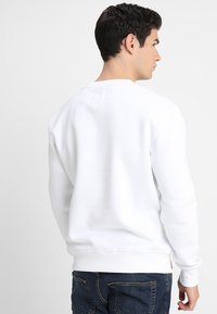 Hvid sweatshirt med rund hals, ribbede ærmer og kant. Har et lille mærke bagpå. Kombinationen er med blå denim jeans.