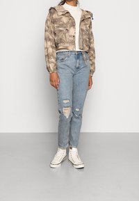 Przycięta kamuflażowa kurtka z zapinanymi na zamek kieszeniami, zestawiona z jasnoniebieskimi znoszonymi dżinsami i białymi trampkami za kostkę.