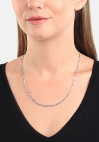 Collar de cadena de plata con eslabones ovalados alargados y diseño retorcido, descansando sobre una blusa negra lisa que resalta su textura.