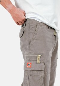 Pantaloni cargo grigio chiaro realizzati in misto cotone. Presentano più tasche, un accento con zip e una patch con logo sul lato.