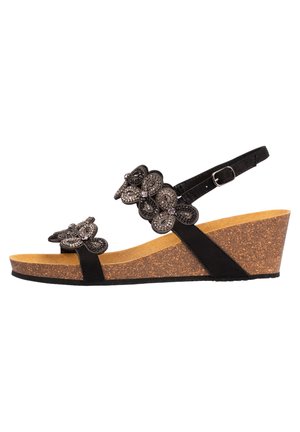 Sandale compensée noire avec des accents floraux décoratifs, sangle de cheville réglable et semelle en liège avec une texture lisse.