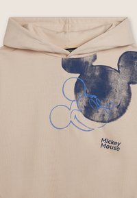 Felpa leggera beige chiaro con una grande grafica blu del volto di Topolino e il suo nome. Il tessuto ha una superficie liscia e un design casual.