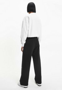 Sudadera corta blanca de manga larga combinada con pantalones deportivos negros holgados, con cintura ajustable y zapatillas blancas.