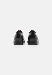 Scarpe eleganti in pelle nera con finitura lucida, dettagli brogue, punta rotonda e tacco impilato, viste da dietro.