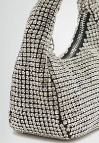 Must musta, millel on selgelt sädelevad rhinestones, struktureeritud kuju, kumer käepide ja tõmblukuga avamine ülevalt.