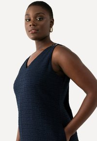 Marineblaues Kleid aus strukturiertem Stoff, V-Ausschnitt und Seitentaschen. Verfügt über dekorative Beschläge an der Schulter. Schlankes, tailliertes Design.