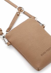 Kožená crossbody taška v tan barvě s texturovaným povrchem, vybavená odnímatelným popruhem, stříbrnými kovovými prvky a vyraženým názvem značky.