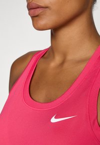 Top sportivo rosa realizzato in tessuto morbido, con scollatura a girocollo e logo Nike bianco sul lato sinistro. Dettaglio ravvicinato della scollatura.