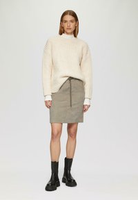 Chunky crèmekleurige gebreide trui met geribbelde textuur, gecombineerd met een grijze corduroy rok met een trekkoord in de taille. Zwarte enkellaarsjes maken de look af.