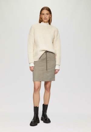 Pull en tricot épais avec texture côtelée, associé à une jupe en velours côtelé grise avec une taille à cordon. Des bottines noires à la cheville complètent le look.