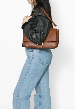 Borsa a tracolla in pelle marrone con finitura testurizzata, forma rettangolare, chiusura in oro, e tracolla removibile, indossata al braccio.