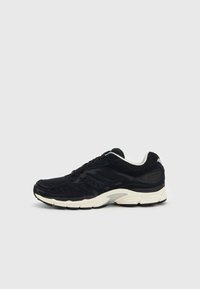 Zapatillas deportivas negras con tejido de malla, superposiciones texturizadas y suela crema. Presentan cordones y un sutil logo en el costado.