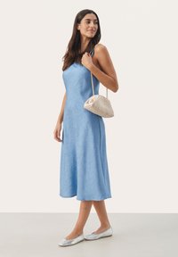 Rochie fără mâneci, de culoare albastru deschis, cu material texturat, cu tiv evazat, asortată cu o geantă împletită crem și balerini argintii.