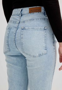 Jeans de denim azul claro con cintura alta, que presentan una etiqueta de cuero marrón con la inscripción "INSIDE" y dos bolsillos traseros.